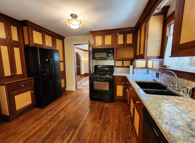 kitchen with light stone counters, black appliances, dark wood-type flooring, and sink