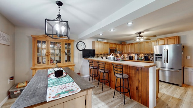 kitchen with stainless steel appliances, backsplash, kitchen peninsula, ceiling fan with notable chandelier, and light wood-type flooring