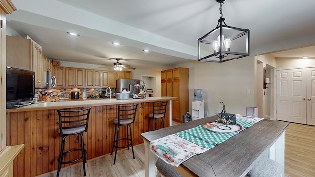 dining area featuring ceiling fan with notable chandelier, light wood-type flooring, and sink