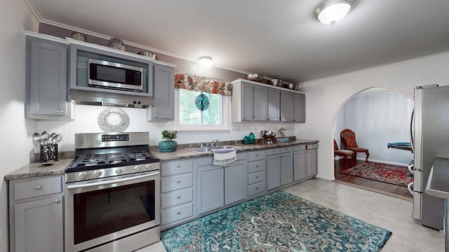 kitchen featuring gray cabinetry, crown molding, stainless steel appliances, and range hood