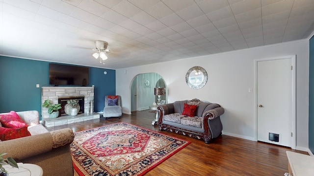 living room featuring ceiling fan, a stone fireplace, dark hardwood / wood-style flooring, and ornamental molding