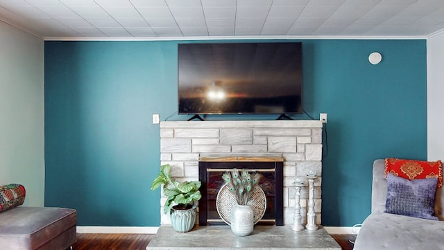 living area with hardwood / wood-style flooring, a stone fireplace, and ornamental molding