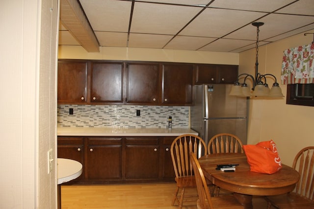 kitchen featuring decorative backsplash, light wood-type flooring, stainless steel refrigerator, and a notable chandelier