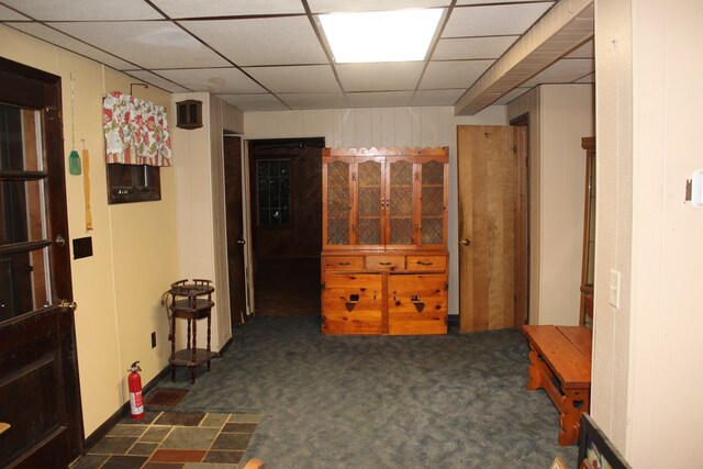 hall featuring dark colored carpet and a paneled ceiling