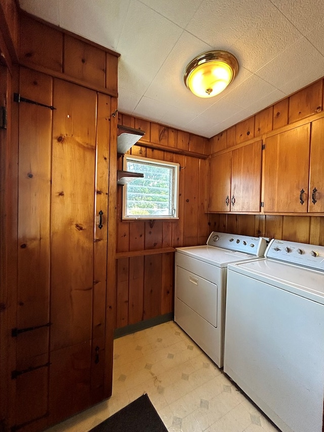 laundry room featuring cabinets, wooden walls, and separate washer and dryer