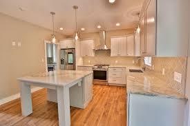 kitchen with wall chimney exhaust hood, stainless steel appliances, a kitchen island, decorative light fixtures, and white cabinets