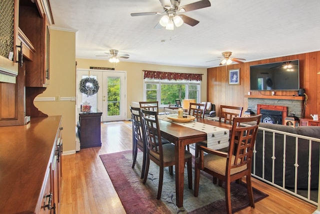 dining area featuring crown molding, wooden walls, light hardwood / wood-style flooring, ceiling fan, and a fireplace