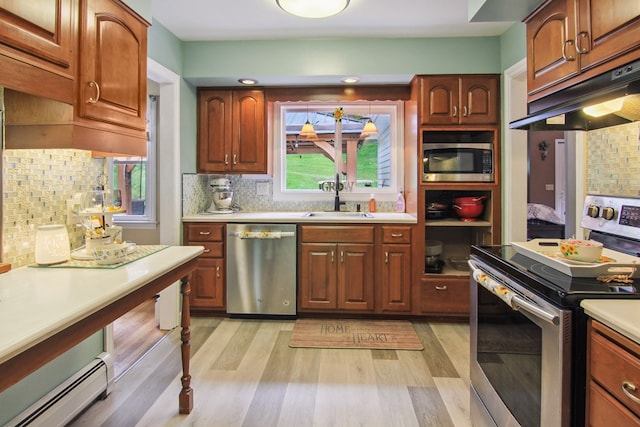 kitchen featuring appliances with stainless steel finishes, light wood-type flooring, backsplash, a baseboard heating unit, and sink