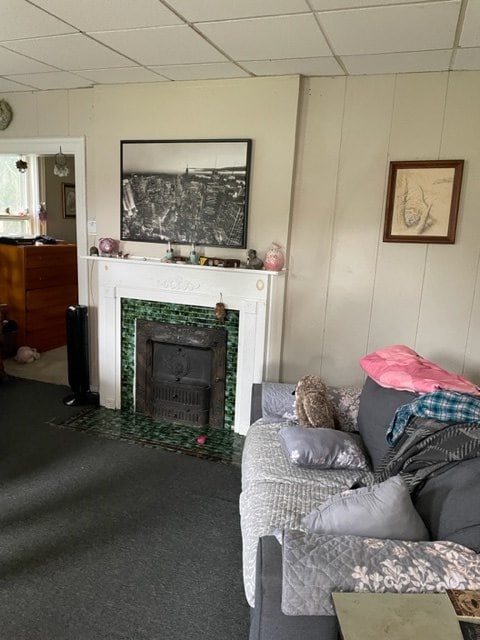 living room featuring a drop ceiling, a tiled fireplace, and carpet