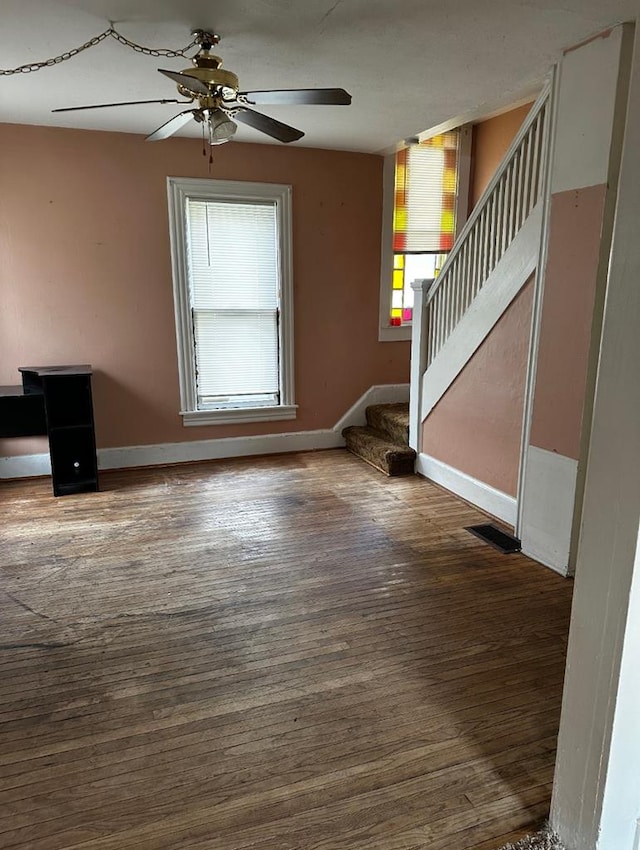 unfurnished living room featuring ceiling fan, a healthy amount of sunlight, and dark wood-type flooring