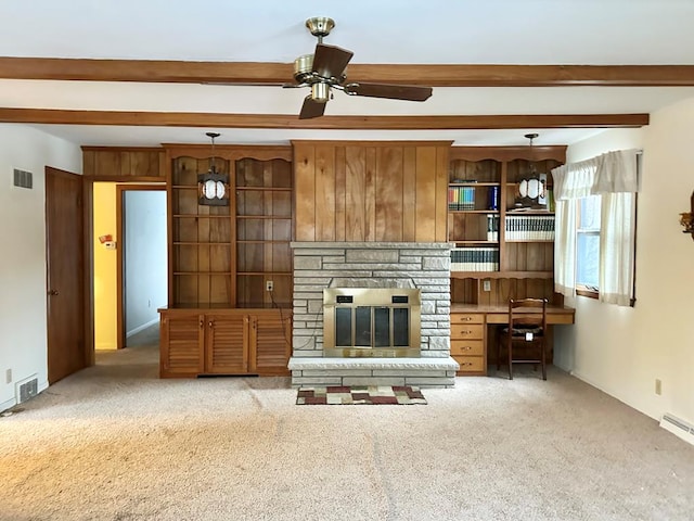 unfurnished living room with ceiling fan, carpet floors, a stone fireplace, beamed ceiling, and wood walls