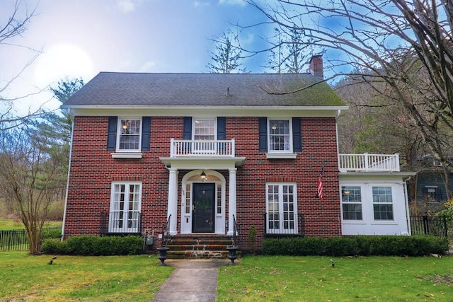 colonial house featuring a balcony and a front lawn