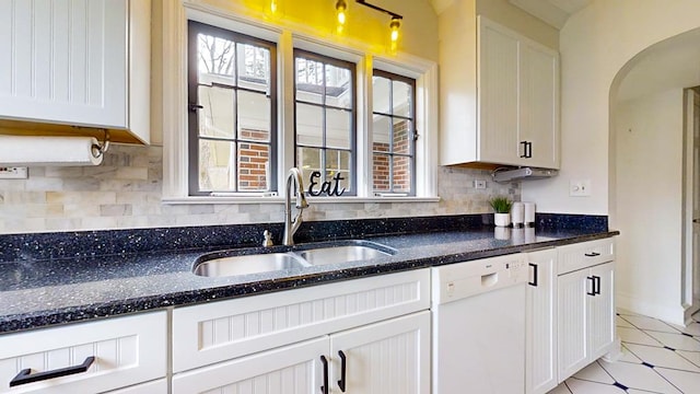 kitchen with white cabinets, white dishwasher, dark stone counters, and sink