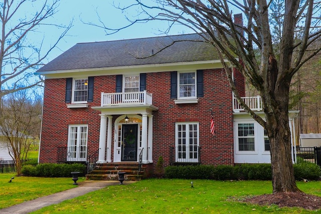 colonial inspired home with a balcony and a front yard