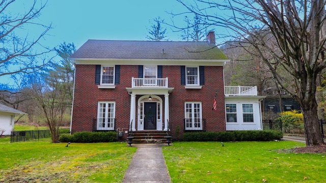 colonial inspired home featuring a balcony and a front lawn