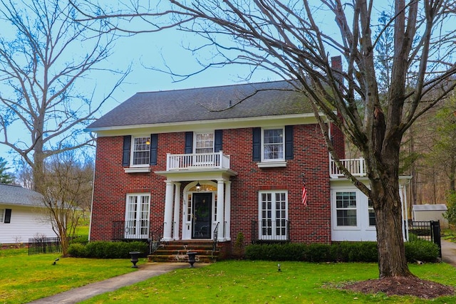 colonial inspired home featuring a balcony and a front yard