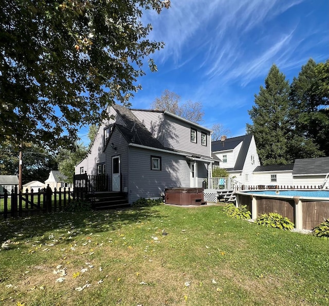 rear view of property featuring a swimming pool with hot tub and a yard