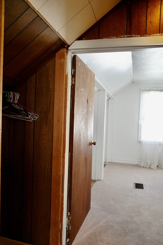 interior space with vaulted ceiling, wooden walls, and light colored carpet