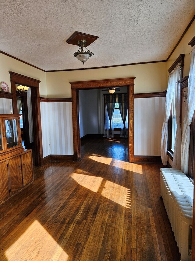 unfurnished living room featuring dark wood-type flooring, ornamental molding, and a textured ceiling