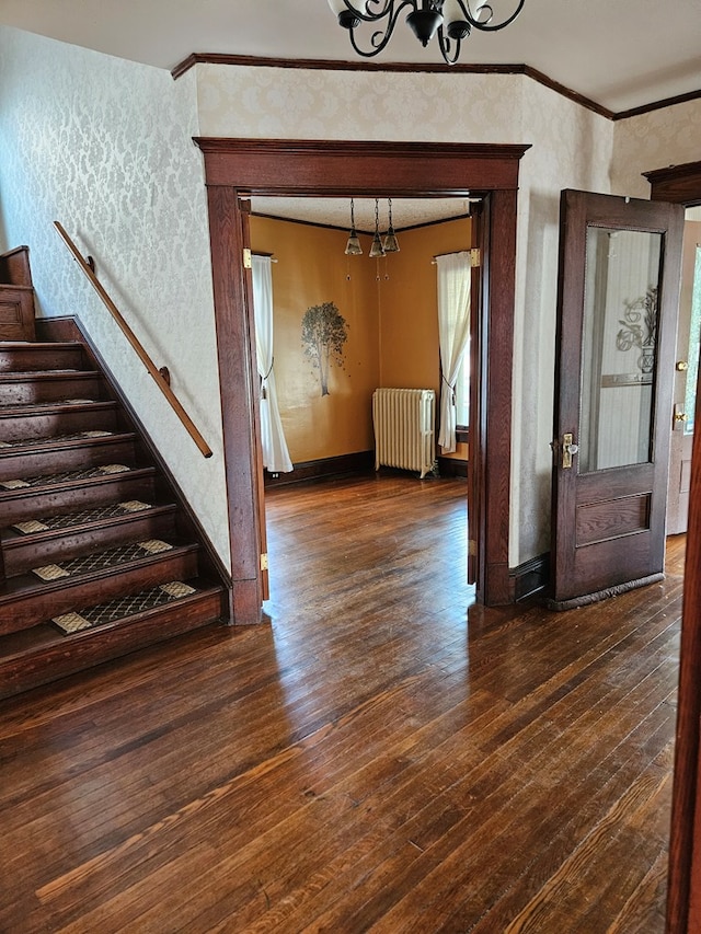 entrance foyer with dark wood-type flooring, ornamental molding, radiator heating unit, and an inviting chandelier