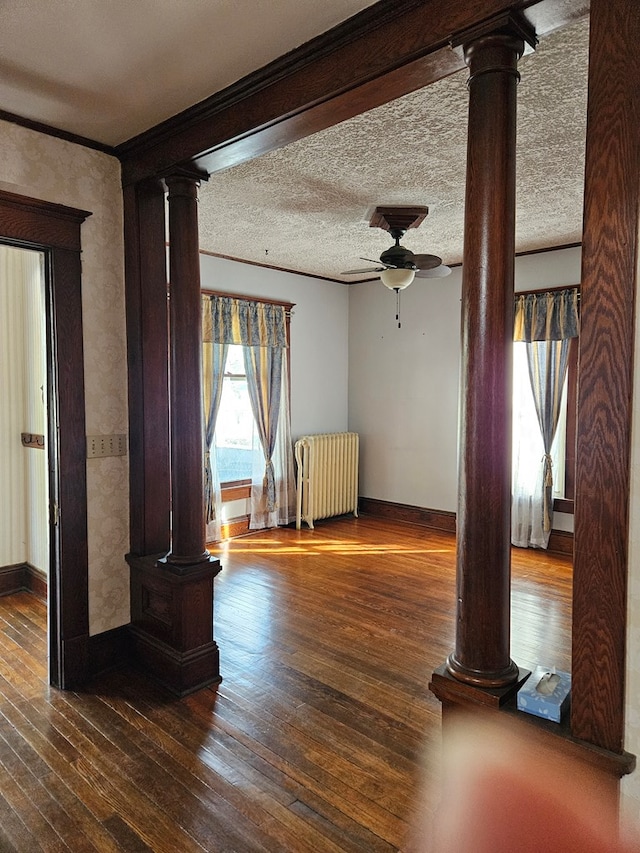 interior space with dark wood-type flooring, ornate columns, ornamental molding, radiator, and ceiling fan