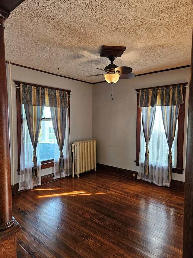 empty room with dark wood-type flooring, ceiling fan, radiator heating unit, a textured ceiling, and ornate columns