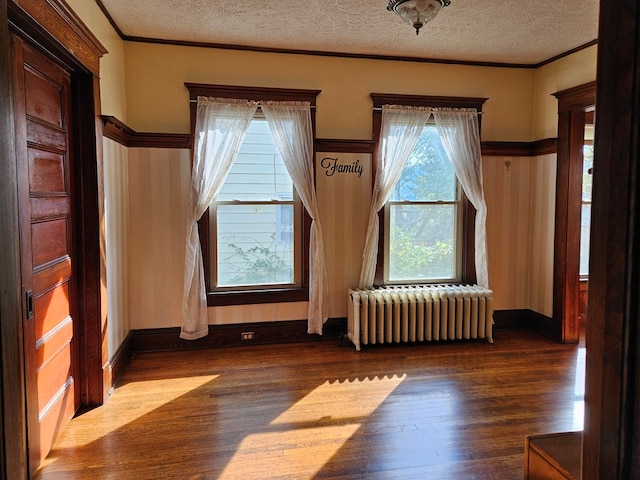 spare room featuring dark wood-type flooring, crown molding, radiator, and a textured ceiling