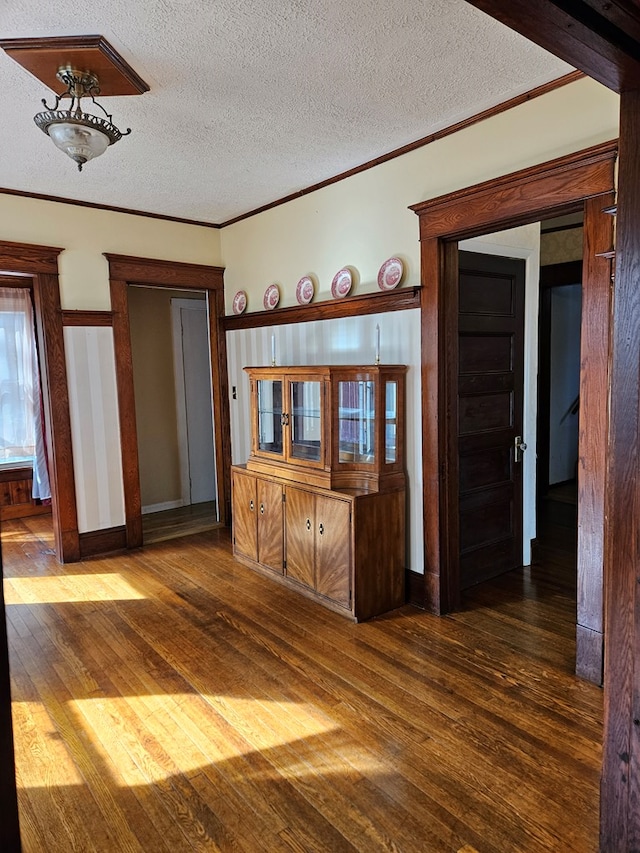 empty room featuring dark wood-type flooring, ornamental molding, and a textured ceiling