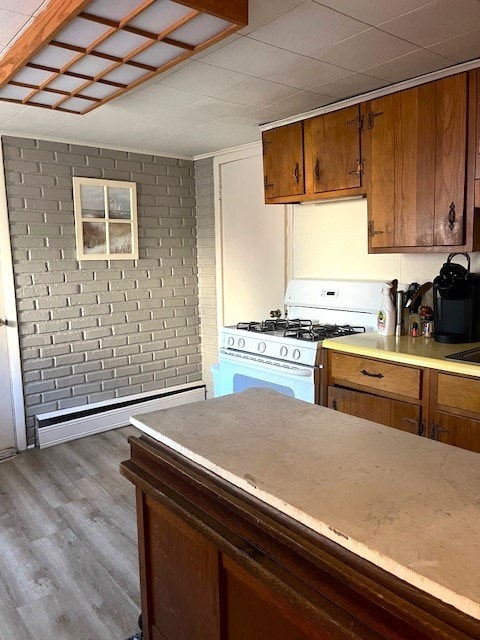 kitchen with light hardwood / wood-style floors, white gas range oven, and brick wall