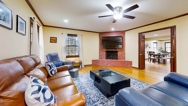 living room with ceiling fan, light hardwood / wood-style floors, crown molding, and a brick fireplace