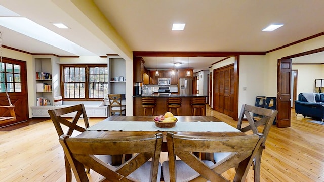 dining room with a healthy amount of sunlight, light wood-type flooring, and ornamental molding