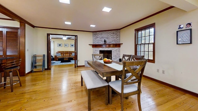 dining space with a brick fireplace, ornamental molding, and light wood-type flooring