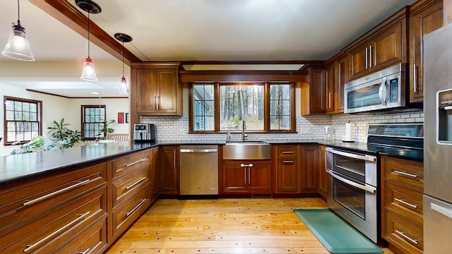 kitchen featuring backsplash, hanging light fixtures, sink, light hardwood / wood-style flooring, and appliances with stainless steel finishes