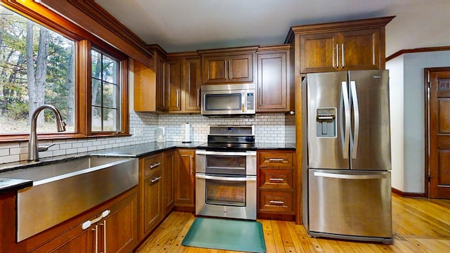 kitchen with decorative backsplash, appliances with stainless steel finishes, light hardwood / wood-style floors, and sink