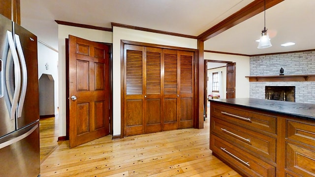 kitchen featuring crown molding, a brick fireplace, decorative light fixtures, light hardwood / wood-style floors, and stainless steel refrigerator