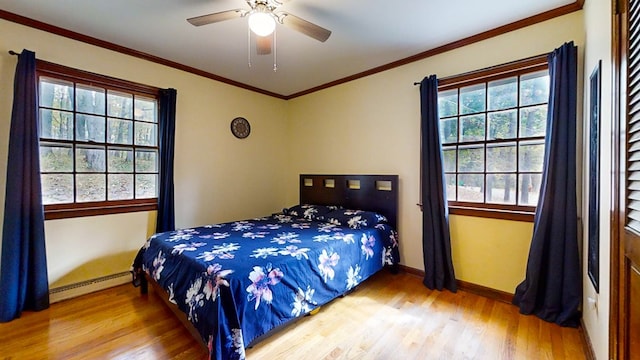 bedroom featuring hardwood / wood-style flooring, baseboard heating, multiple windows, and ceiling fan