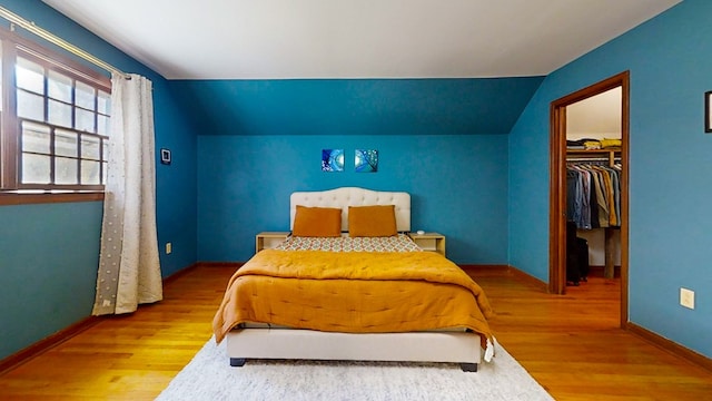 bedroom featuring a spacious closet, a closet, lofted ceiling, and hardwood / wood-style flooring