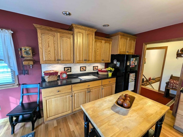 kitchen featuring light wood-type flooring, black refrigerator, and decorative backsplash