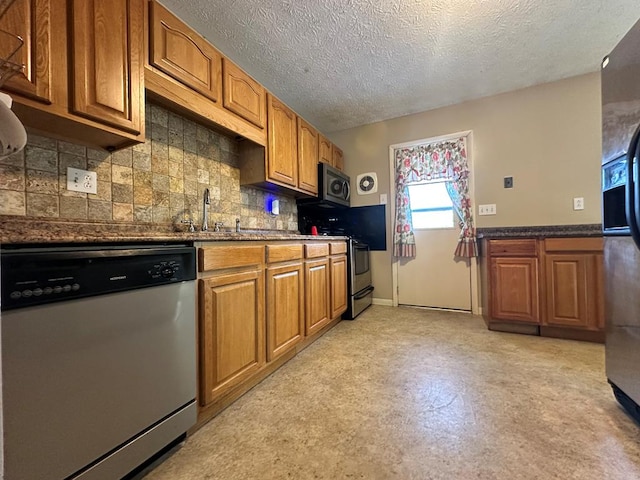 kitchen featuring decorative backsplash, dark stone counters, a textured ceiling, stainless steel appliances, and sink