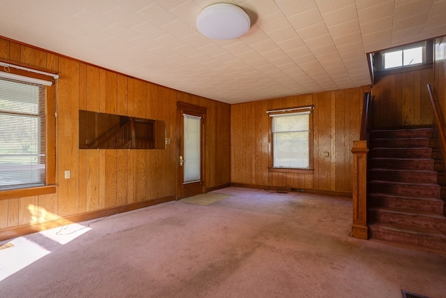 unfurnished living room with light colored carpet, a healthy amount of sunlight, and wood walls