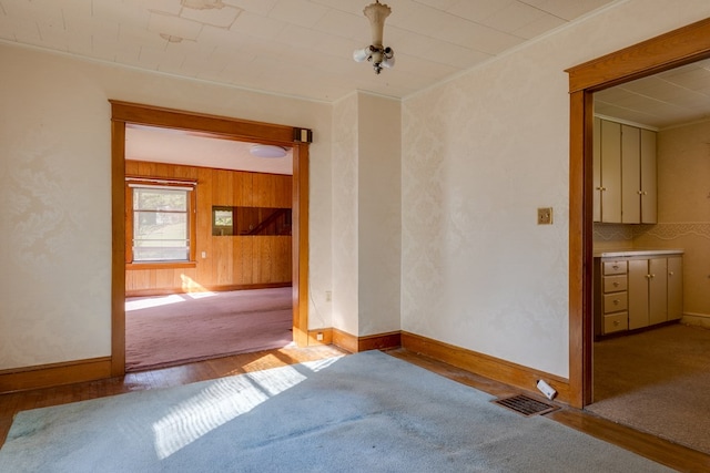 spare room featuring ornamental molding, wooden walls, and light hardwood / wood-style flooring