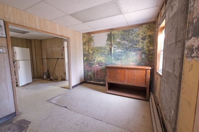 interior space featuring a paneled ceiling, wooden walls, and baseboard heating