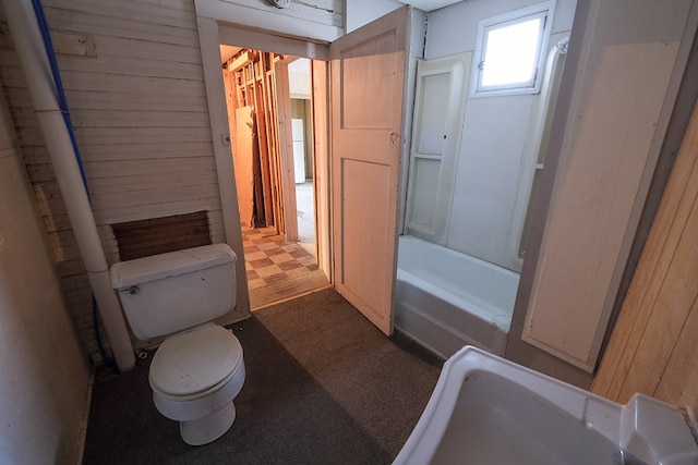 bathroom with a tub to relax in, toilet, and wood walls