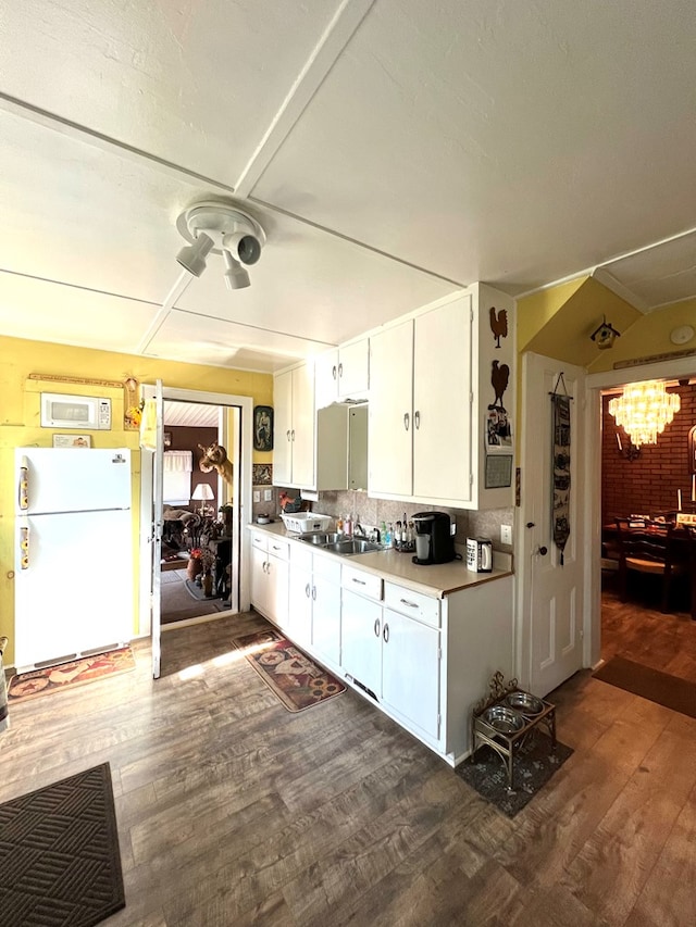 kitchen with white appliances, backsplash, white cabinets, dark wood-type flooring, and an inviting chandelier