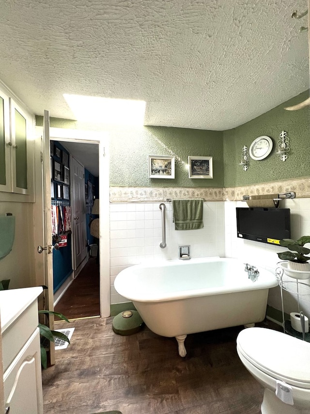 bathroom with toilet, a textured ceiling, wood-type flooring, and a bath