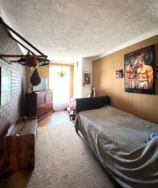 bedroom with hardwood / wood-style floors, a textured ceiling, and brick wall