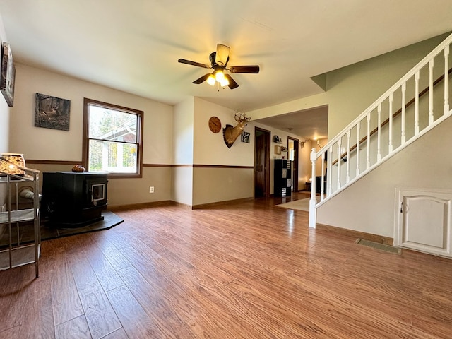 unfurnished living room featuring hardwood / wood-style floors, a wood stove, and ceiling fan