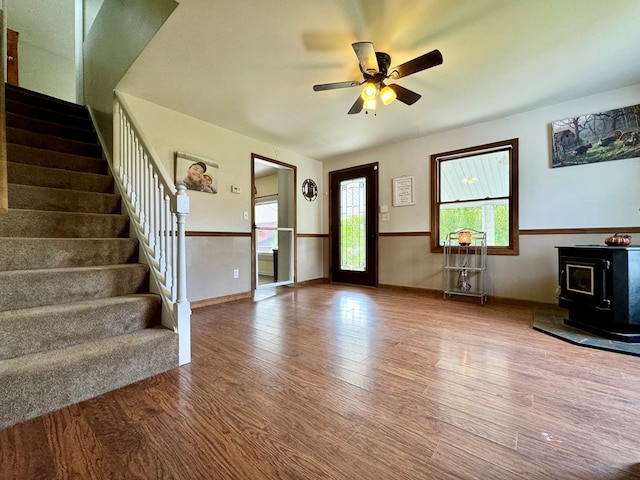 unfurnished living room featuring a wood stove, ceiling fan, and hardwood / wood-style floors