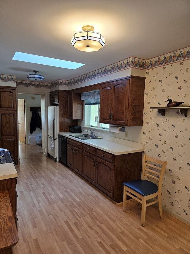 kitchen featuring a skylight, dark brown cabinets, light hardwood / wood-style flooring, dishwasher, and stainless steel refrigerator