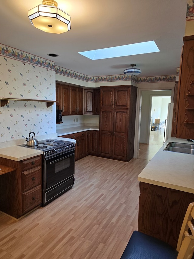 kitchen featuring black range, light wood-type flooring, sink, and a skylight